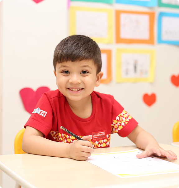 Menino sorridente sentado em mesa escolar da Canadian Global School